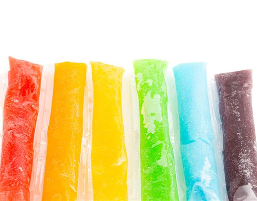 Six colorful frozen ice pops in plastic sleeves arranged side by side, in red, orange, yellow, green, blue, and purple hues against a white background.
