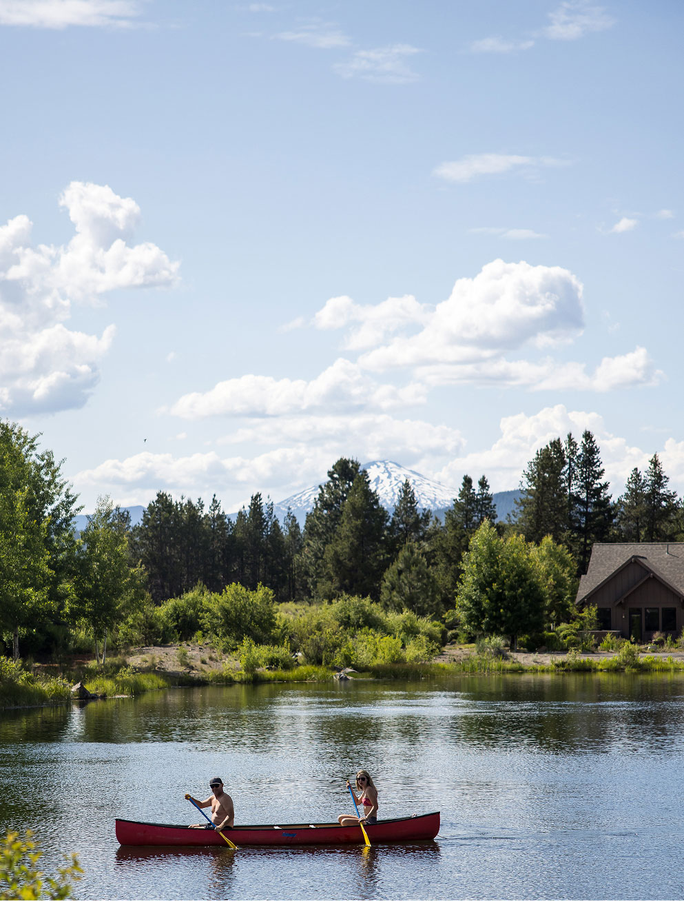 two women rowing a canoe on a lake surrounded by mountains on a clear day