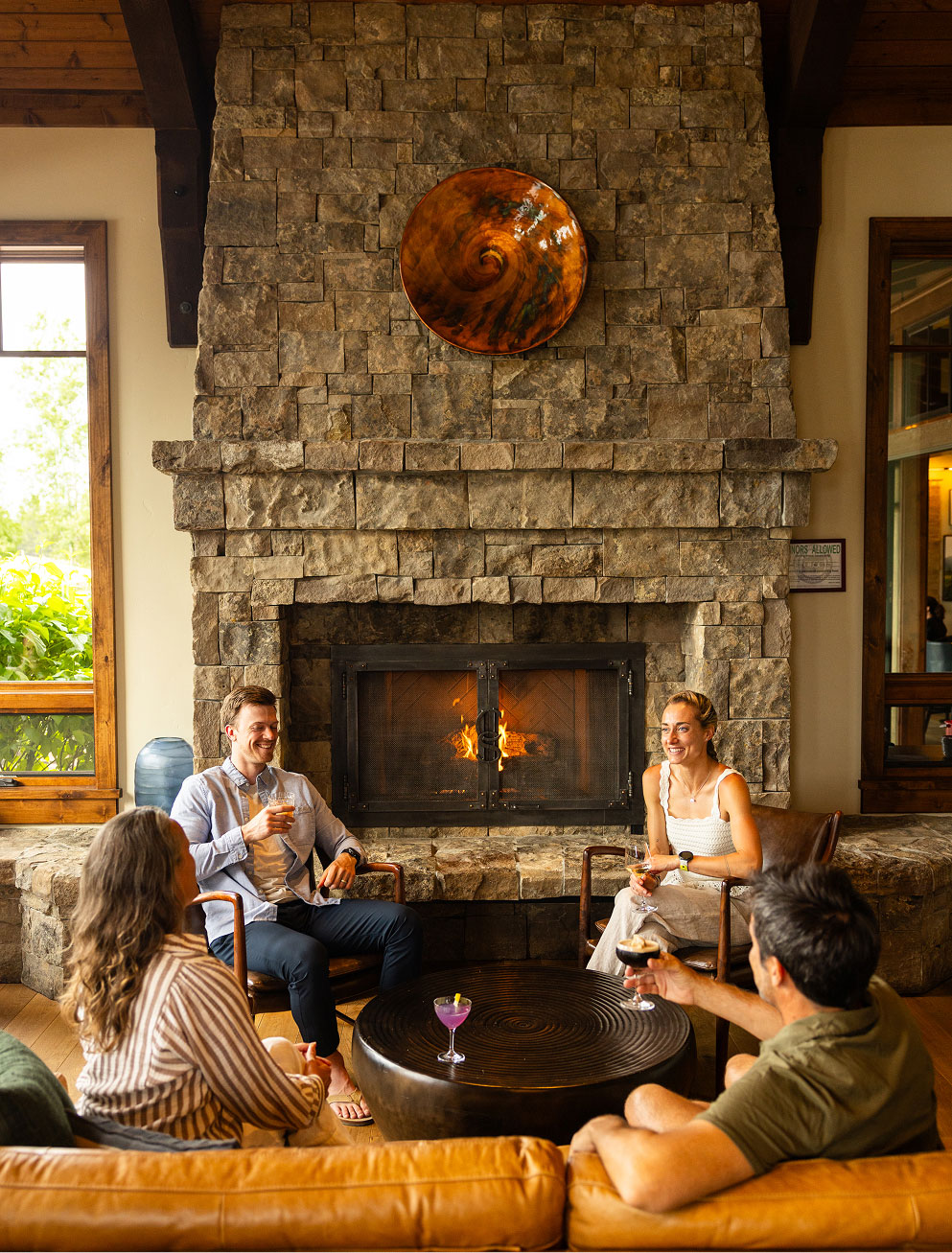 a group of men and women gathered seated in front of a large stone fireplace